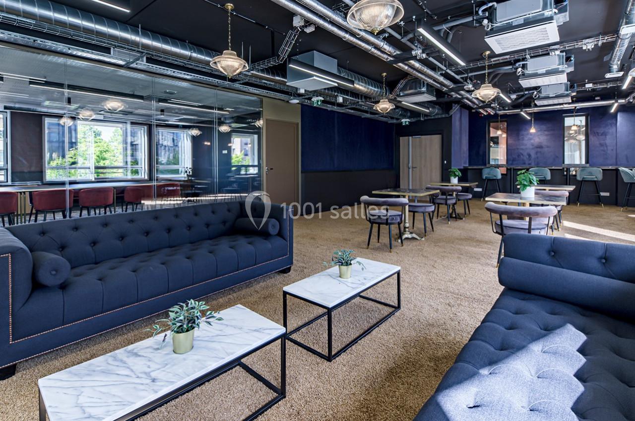 Espace intérieur moderne avec canapés bleus, tables basses en marbre, et grandes baies vitrées laissant entrer la lumière.