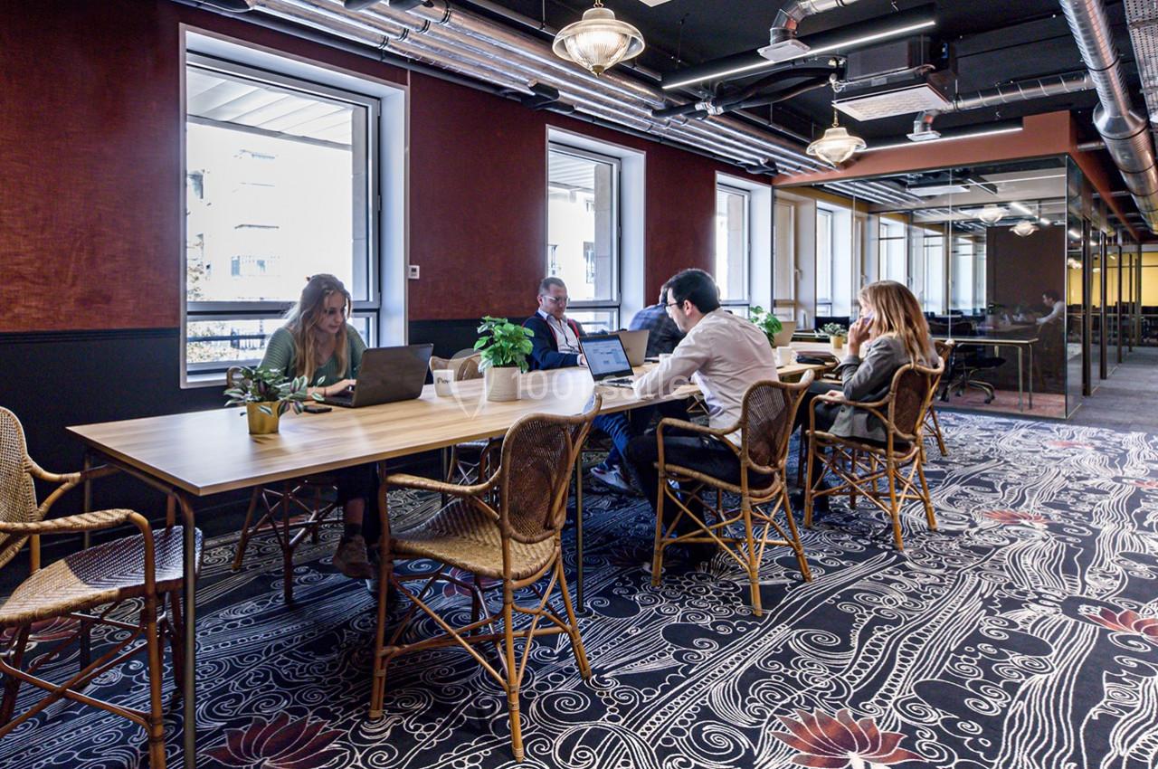 Personnes travaillant sur des ordinateurs portables autour d'une grande table dans un espace de coworking lumineux et décoré.