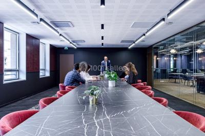 Salle de réunion moderne avec table en verre, chaises violettes, écran mural et fenêtres laissant entrer la lumière…
