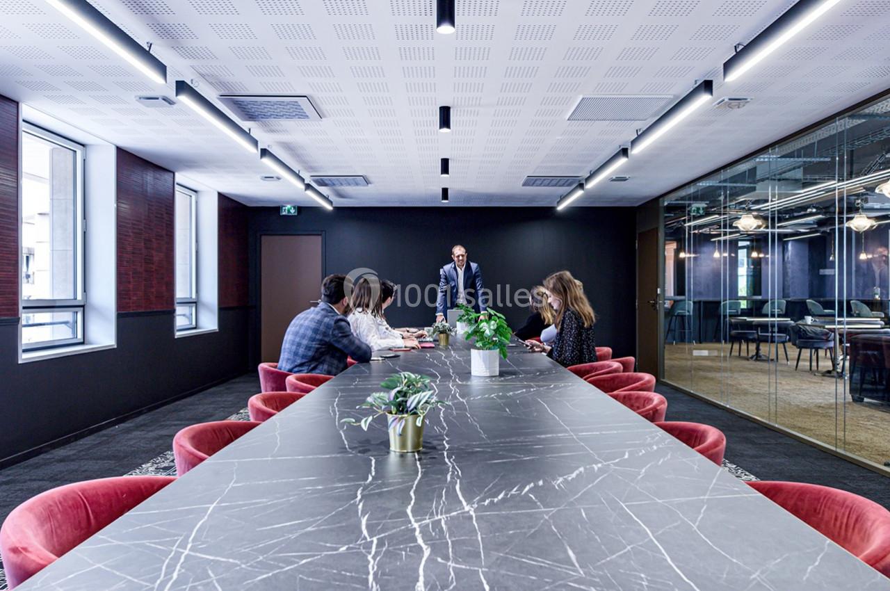 Salle de réunion moderne avec une grande table en marbre, des chaises rouges et un groupe de personnes en discussion.