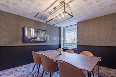Salle de réunion moderne avec table en verre, chaises violettes, écran mural et fenêtres laissant entrer la lumière…