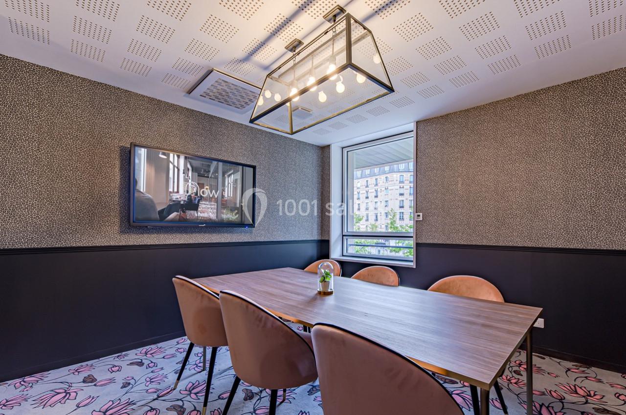 Salle de réunion moderne avec table en bois, chaises rembourrées, écran mural et grande fenêtre donnant sur l'extérieur.