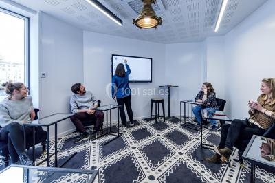 Salle de réunion moderne avec table en verre, chaises violettes, écran mural et fenêtres laissant entrer la lumière…