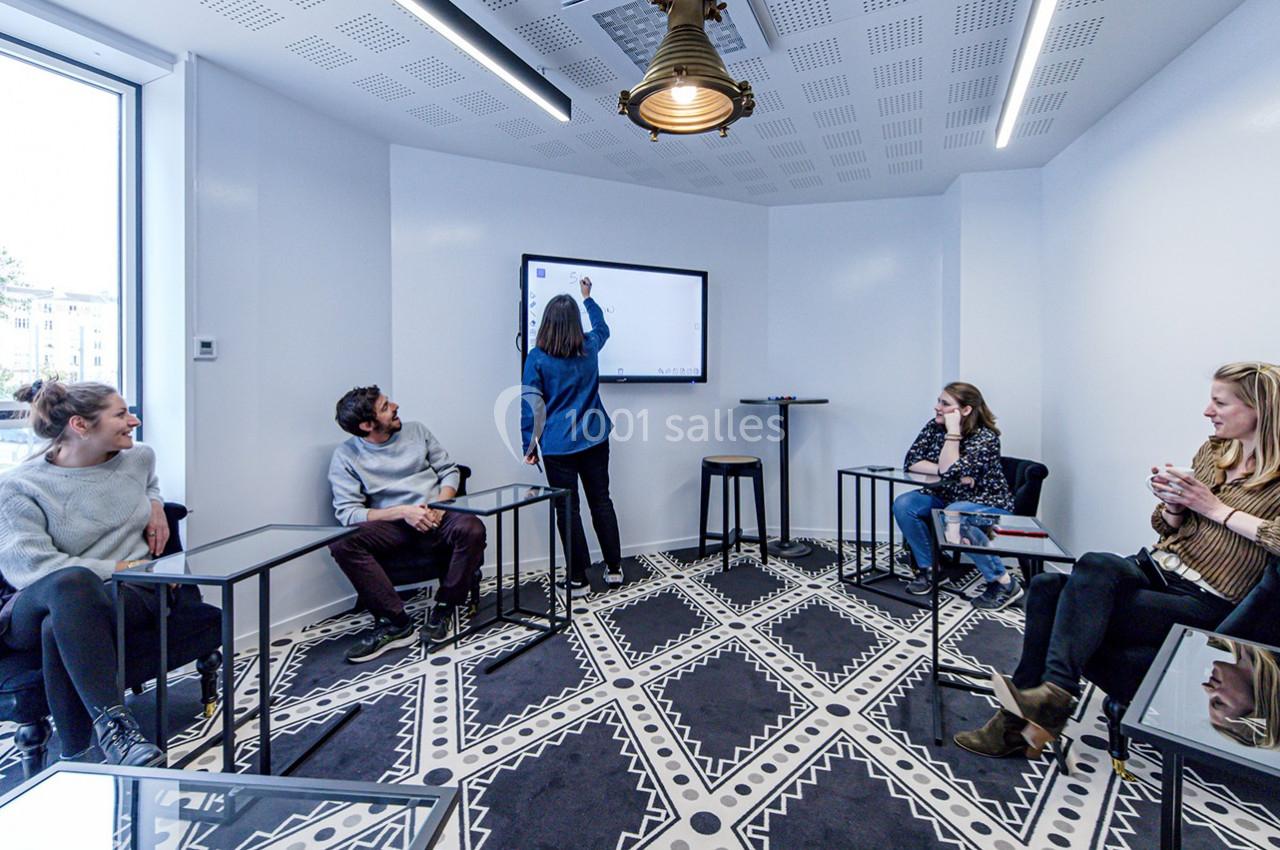Quatre personnes assises et une debout devant un écran interactif dans une salle de réunion lumineuse.