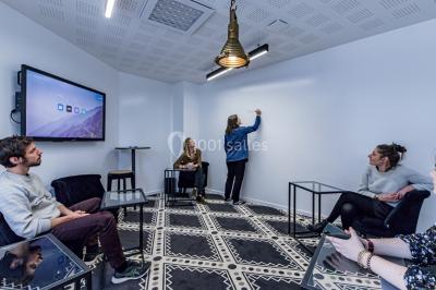 Salle de réunion moderne avec table en verre, chaises violettes, écran mural et fenêtres laissant entrer la lumière…