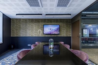 Salle de réunion moderne avec table en verre, chaises violettes, écran mural et fenêtres laissant entrer la lumière…