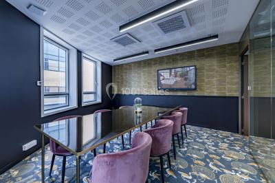 Salle de réunion moderne avec table en verre, chaises violettes, écran mural et fenêtres laissant entrer la lumière…