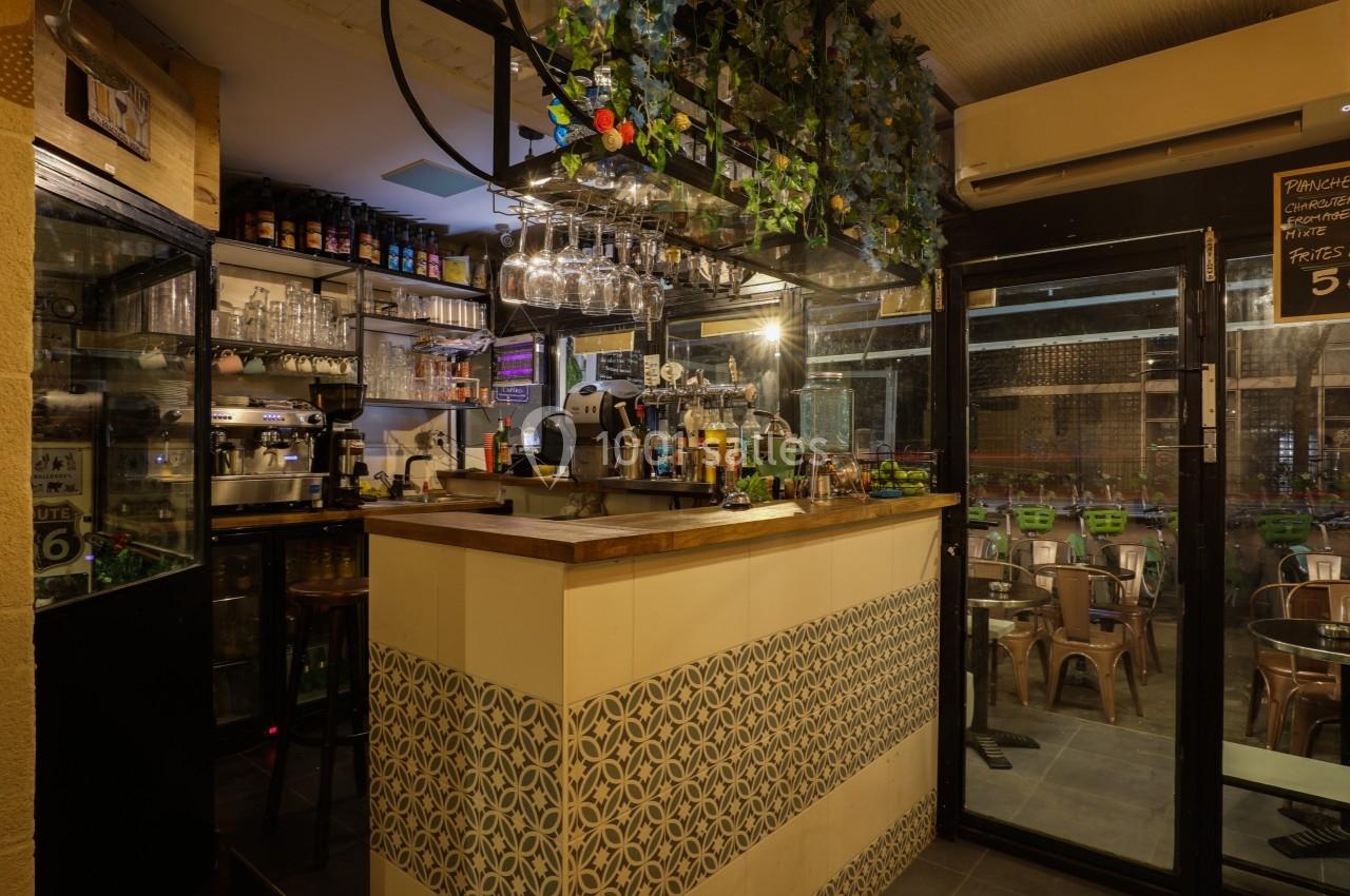 Comptoir de bar avec machine à café, verres suspendus et décoration végétale, donnant sur une terrasse extérieure.