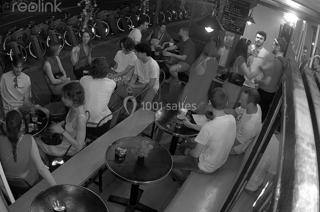 Des personnes discutent et partagent un moment convivial dans un bar animé, capturé en noir et blanc.