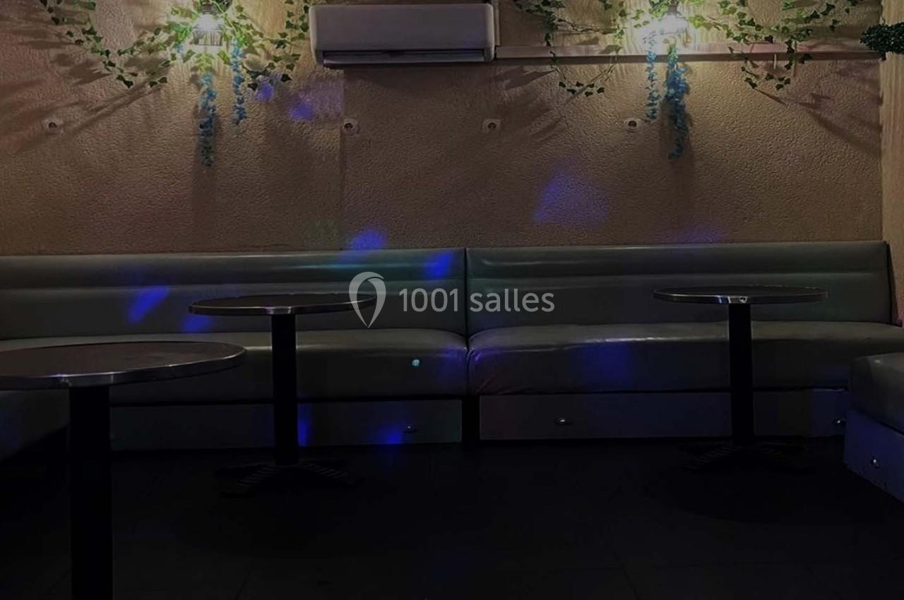 Banquettes grises et tables rondes dans une pièce sombre avec éclairage tamisé et décorations végétales murales.