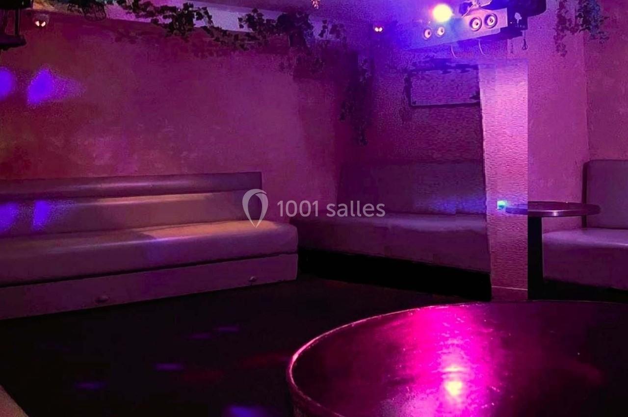 Salle vide avec banquettes, murs roses, lumière tamisée et reflets violets, ambiance de club ou bar lounge.