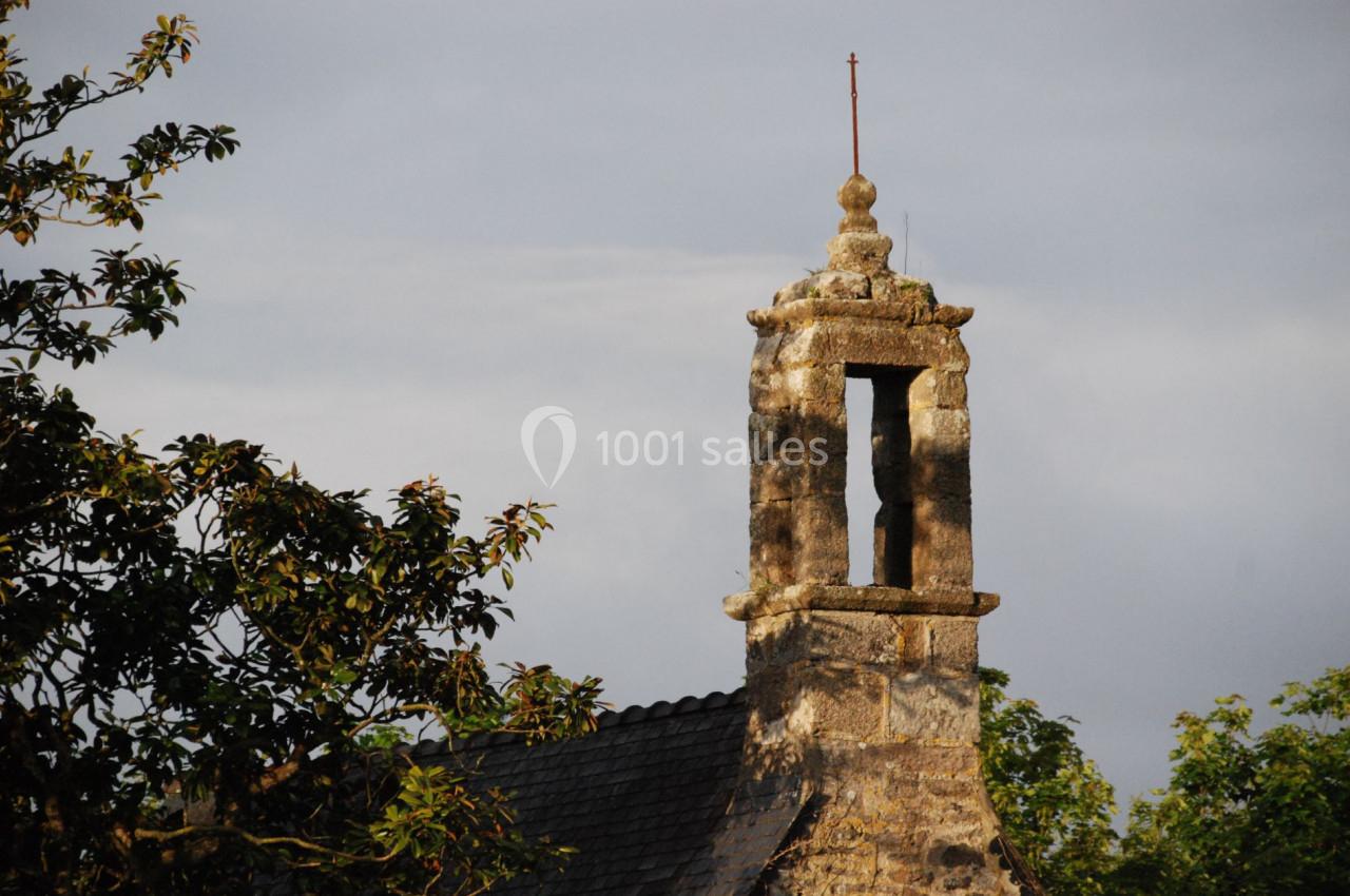Clocher en pierre d'une petite chapelle entourée de feuillage, éclairé par une lumière douce en fin de journée.