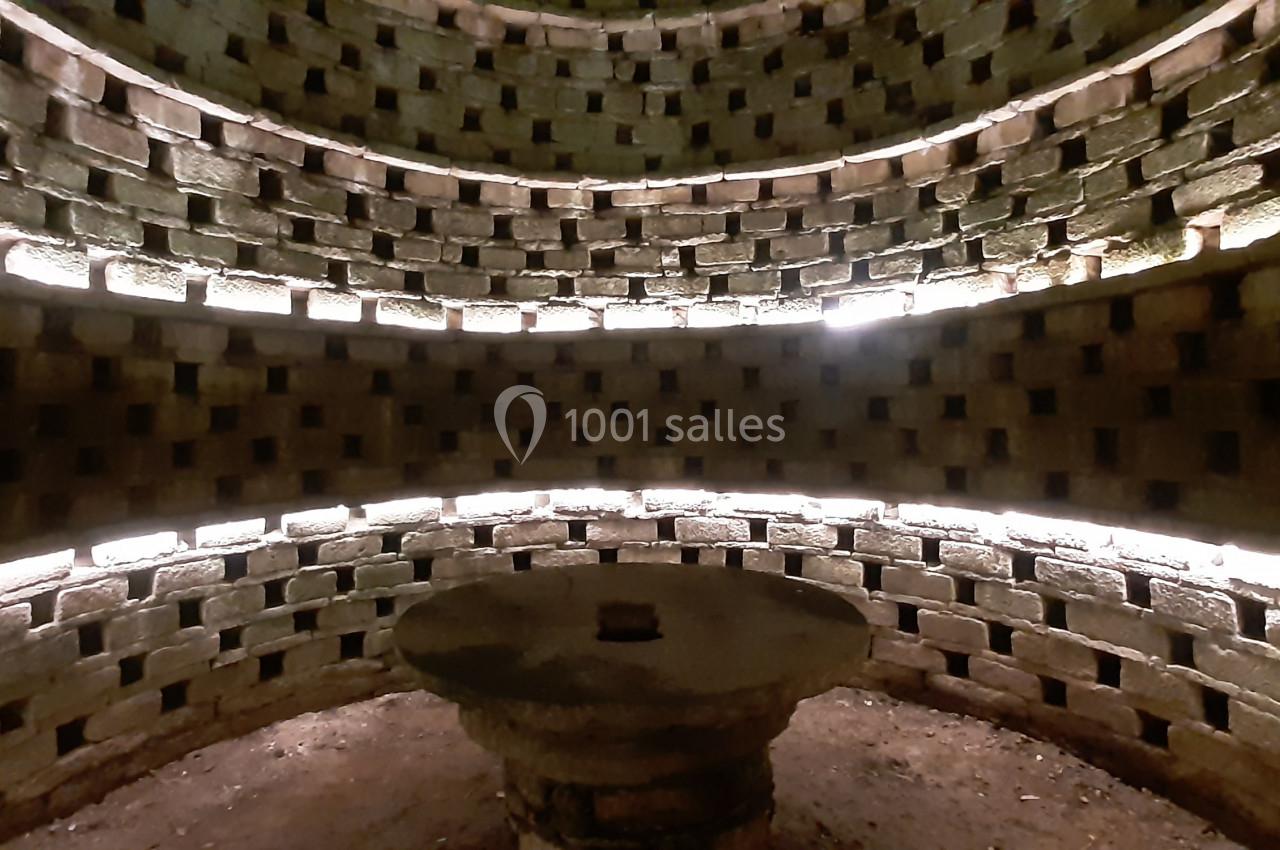 Mur circulaire en briques avec des ouvertures régulières, éclairé par des lumières, entourant une structure centrale en…