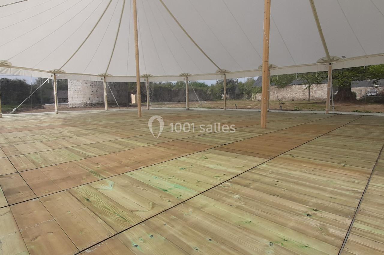 Intérieur d'une tente avec un sol en bois clair, entourée de parois transparentes et située dans un espace extérieur…