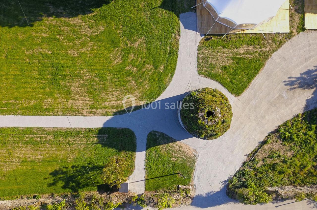 Vue aérienne d'un chemin en croix entouré de pelouses, avec une structure circulaire végétalisée au centre.