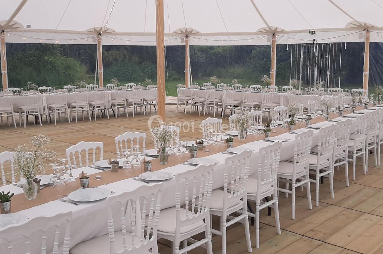 Tables longues décorées de nappes blanches et chaises assorties sous une tente ouverte, prêtes pour un événement.