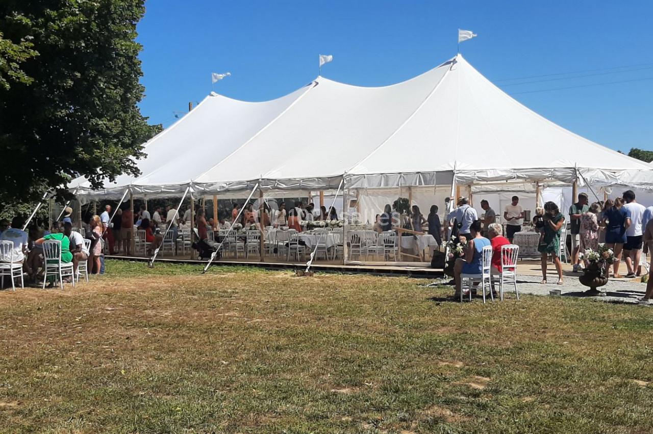 Grande tente blanche installée en extérieur, entourée de personnes debout et assises lors d'un événement par temps…