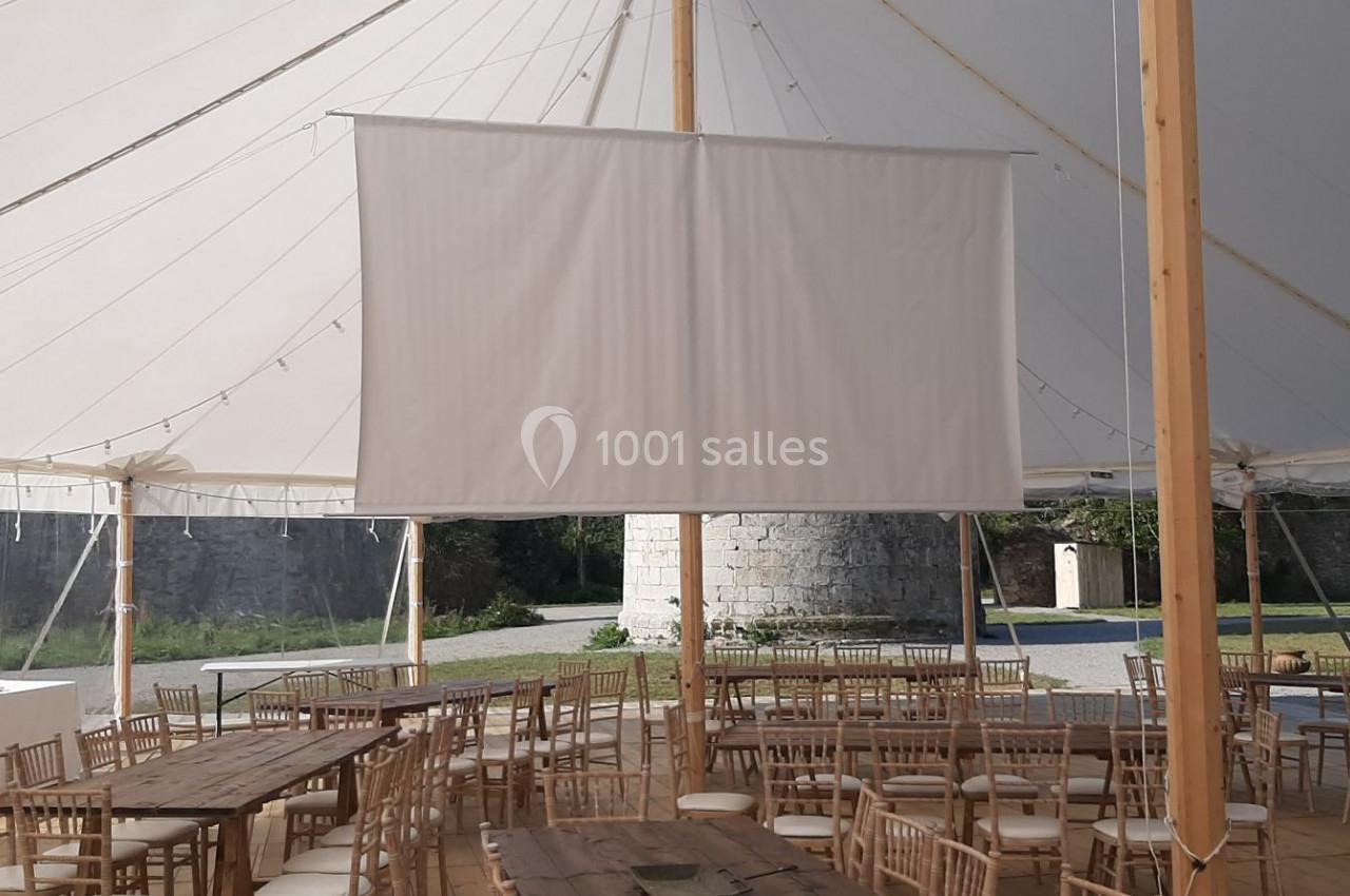 Intérieur d'une tente avec tables en bois, chaises et un écran blanc suspendu, installé dans un espace extérieur.
