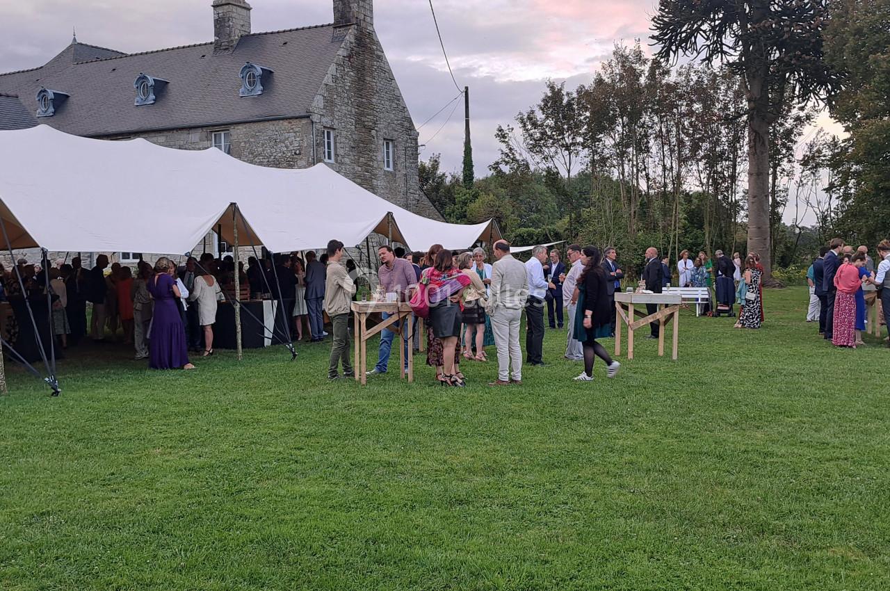 Groupe de personnes rassemblées sous une tente blanche dans un jardin près d'un bâtiment en pierre.