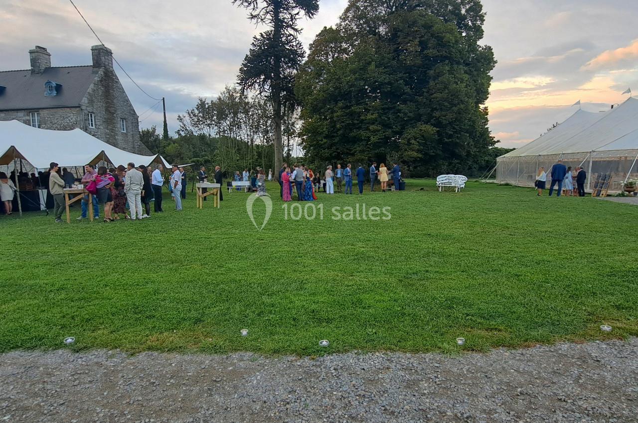 Personnes rassemblées sur une pelouse devant un manoir, avec des tentes blanches installées pour un événement en plein air.