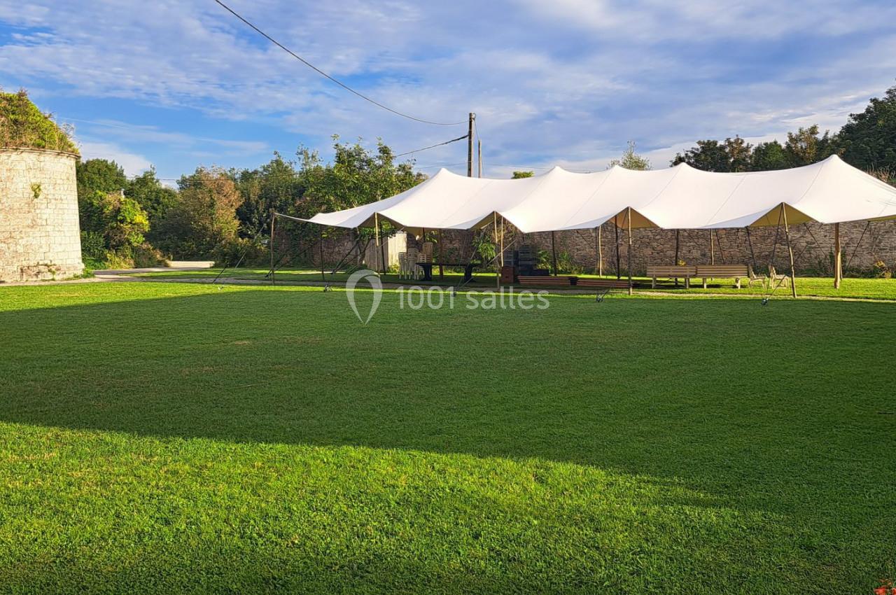 Grande pelouse avec une tente blanche tendue près d'une tour en pierre recouverte de végétation.