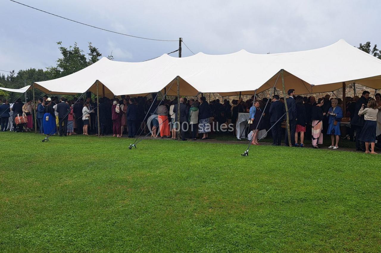 Un grand groupe de personnes rassemblées sous une tente blanche dans un espace extérieur herbeux.