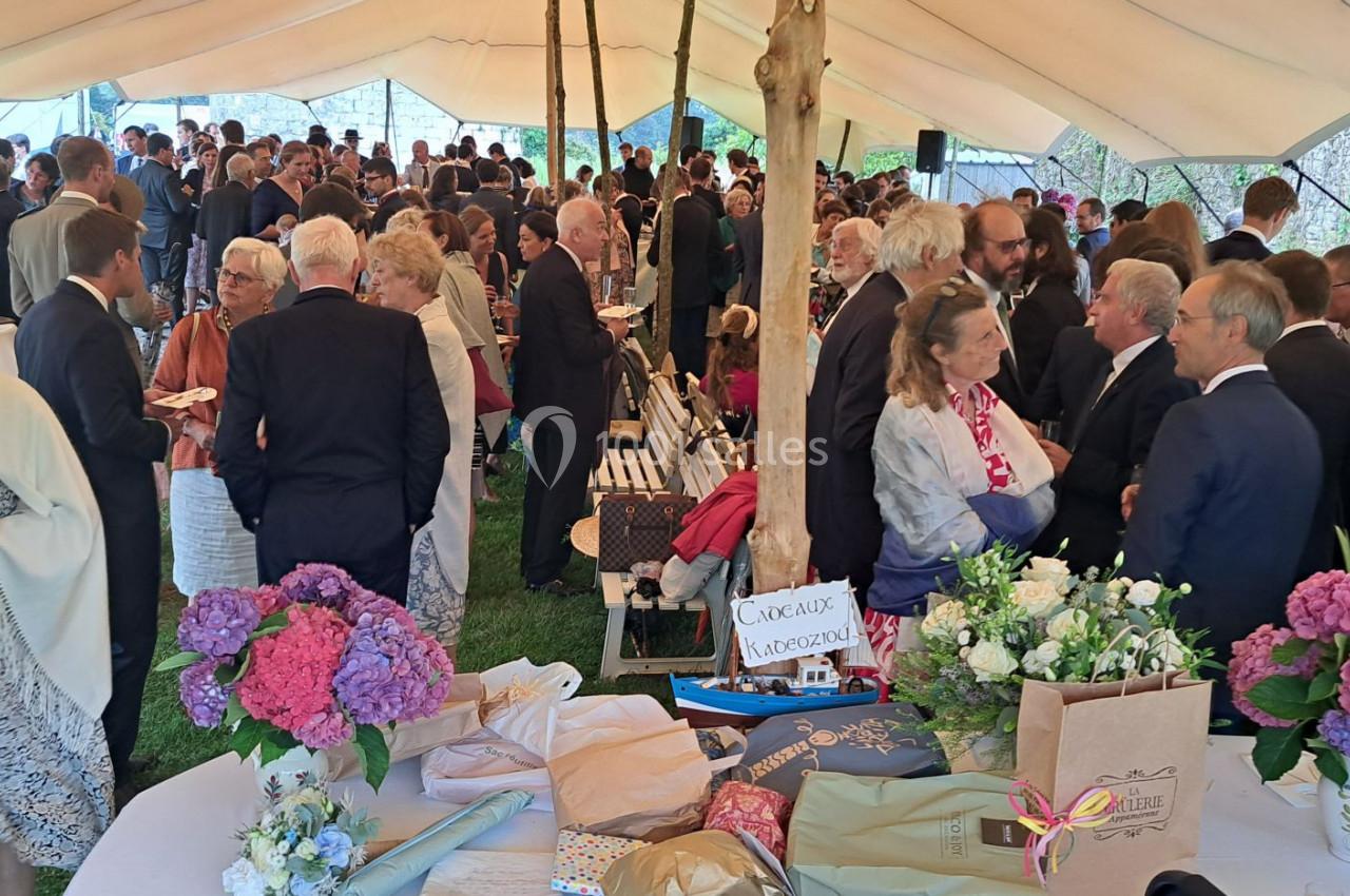 Groupe de personnes rassemblées sous une grande tente lors d'un événement, entourées de décorations florales et de tables.