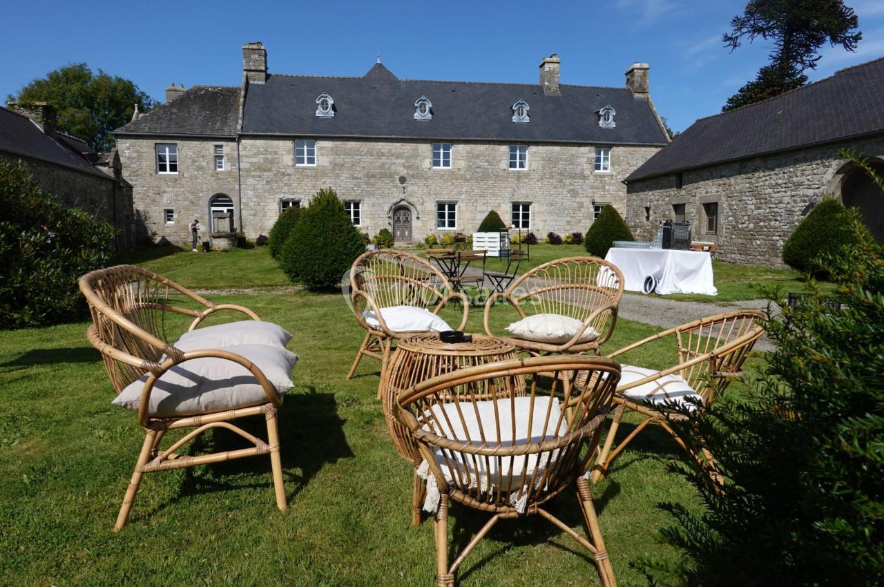 Fauteuils en rotin disposés sur une pelouse devant une grande bâtisse en pierre sous un ciel bleu.