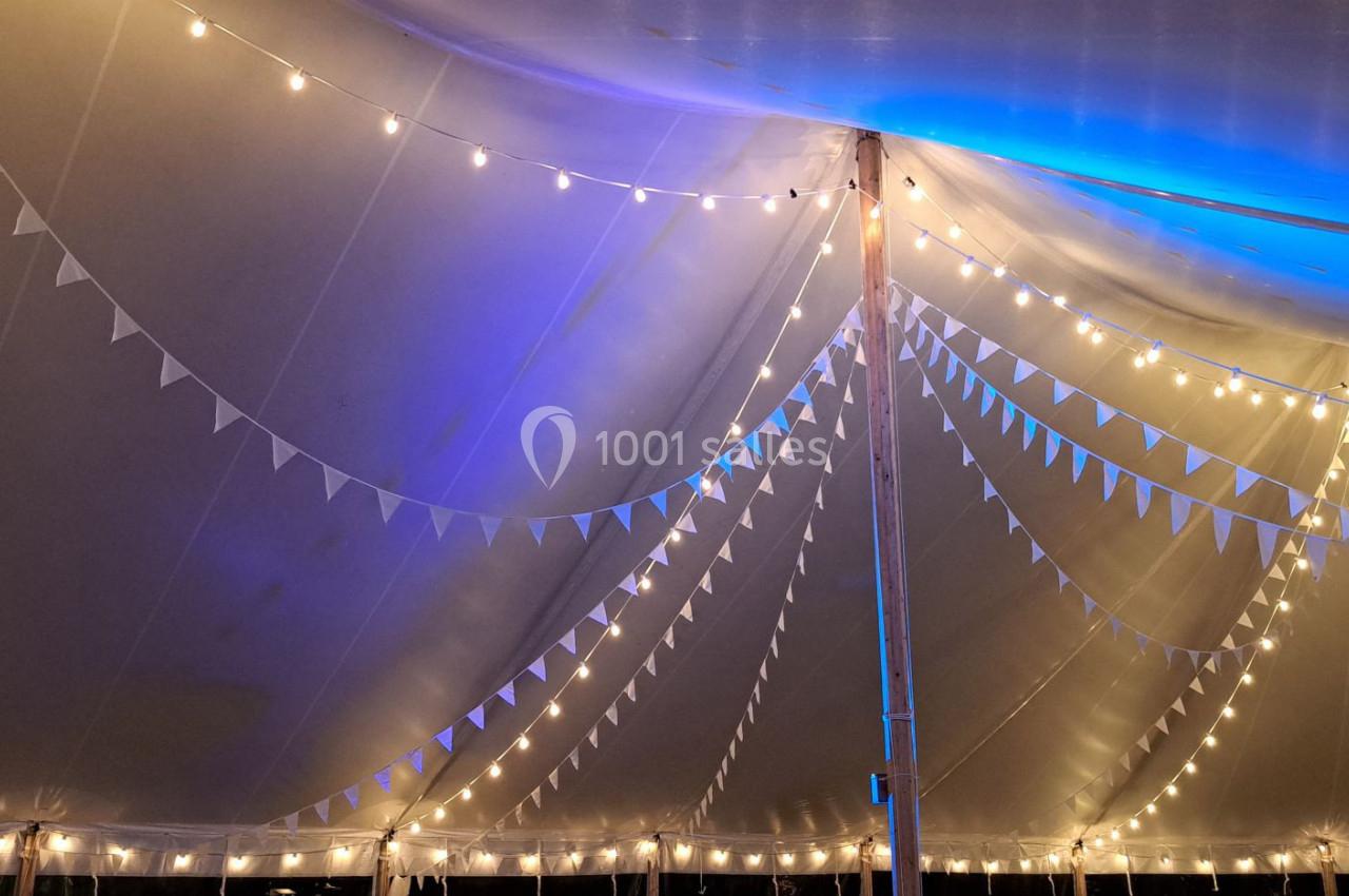 Guirlandes lumineuses suspendues sous une tente blanche avec des fanions triangulaires et un éclairage bleu.