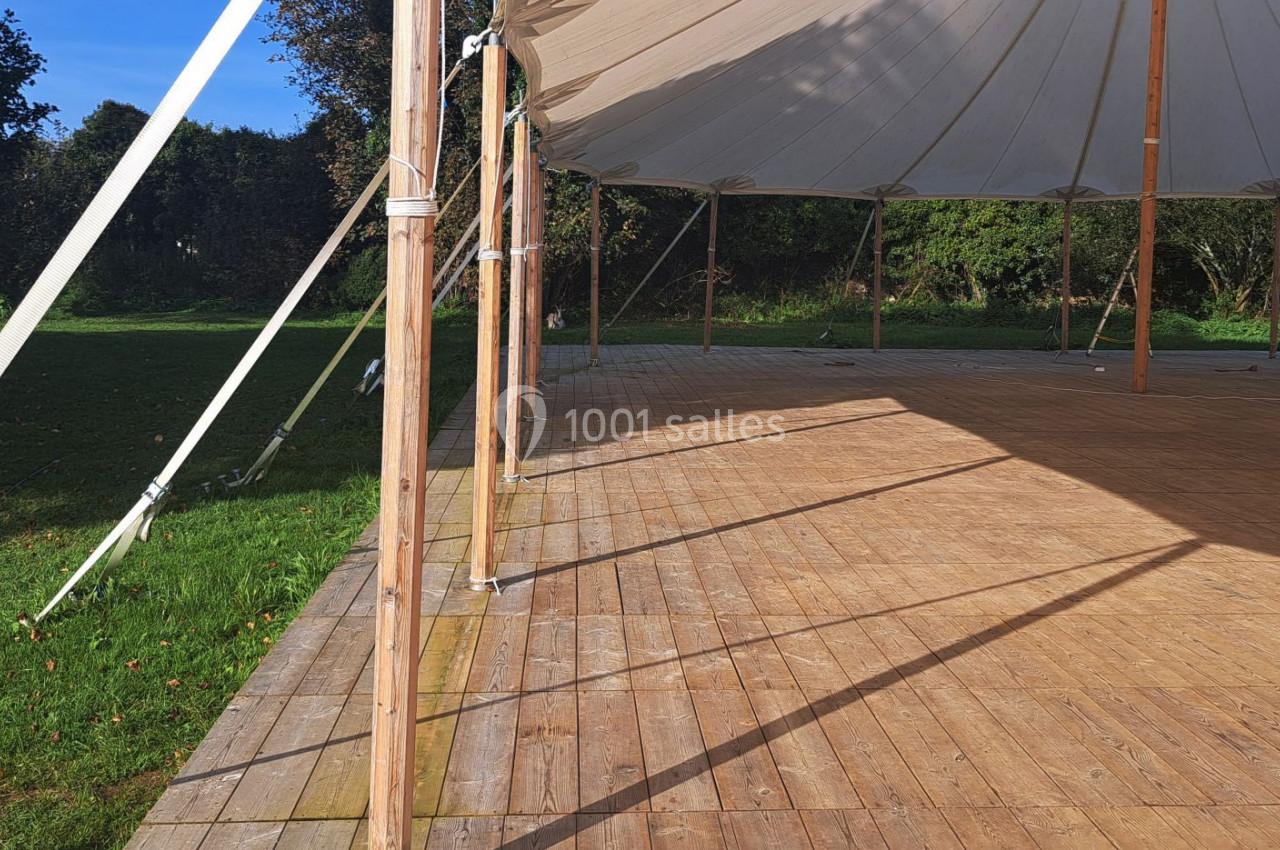 Structure en bois avec un toit tendu, installée dans un espace extérieur verdoyant et ensoleillé.