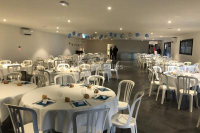 Salle de réception lumineuse avec tables rondes décorées de nappes blanches, fleurs et vaisselle élégante.