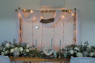 Salle de réception lumineuse avec tables rondes décorées de nappes blanches, fleurs et vaisselle élégante.