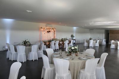 Salle de réception lumineuse avec tables rondes décorées de nappes blanches, fleurs et vaisselle élégante.