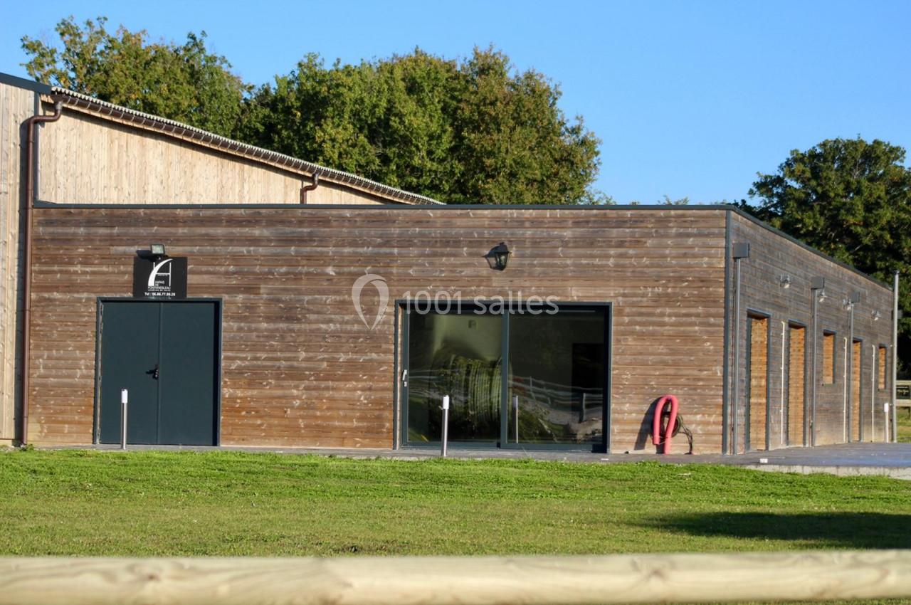 Bâtiment en bois avec portes vitrées et entrée principale, entouré de pelouse et d'arbres en arrière-plan.