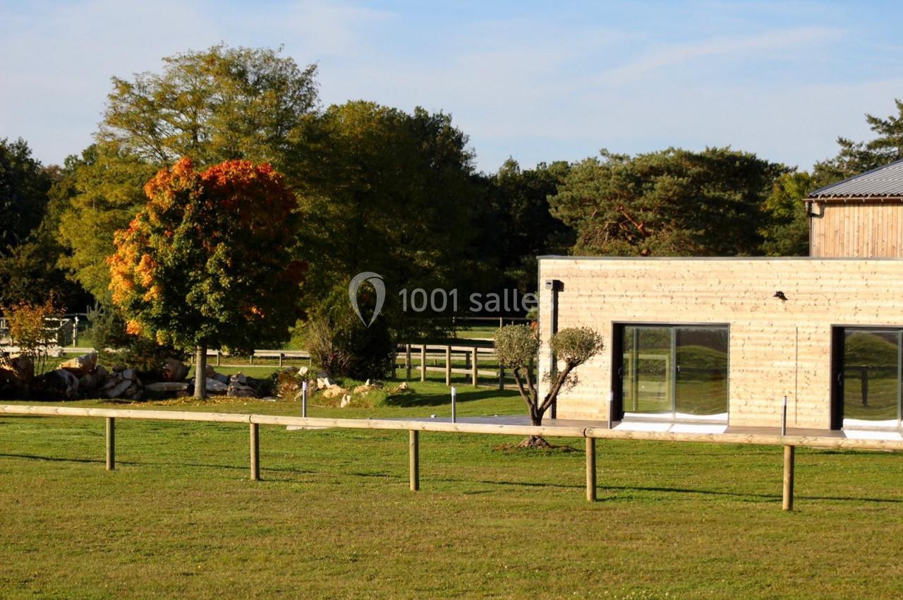 Bâtiment en bois moderne entouré d'une pelouse, avec un arbre aux feuilles d'automne et une clôture en premier plan.