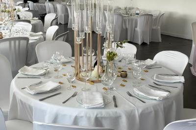 Salle de réception lumineuse avec tables rondes décorées de nappes blanches, fleurs et vaisselle élégante.