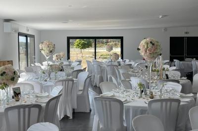 Salle de réception lumineuse avec tables rondes décorées de nappes blanches, fleurs et vaisselle élégante.