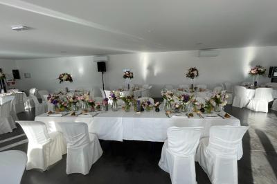 Salle de réception lumineuse avec tables rondes décorées de nappes blanches, fleurs et vaisselle élégante.
