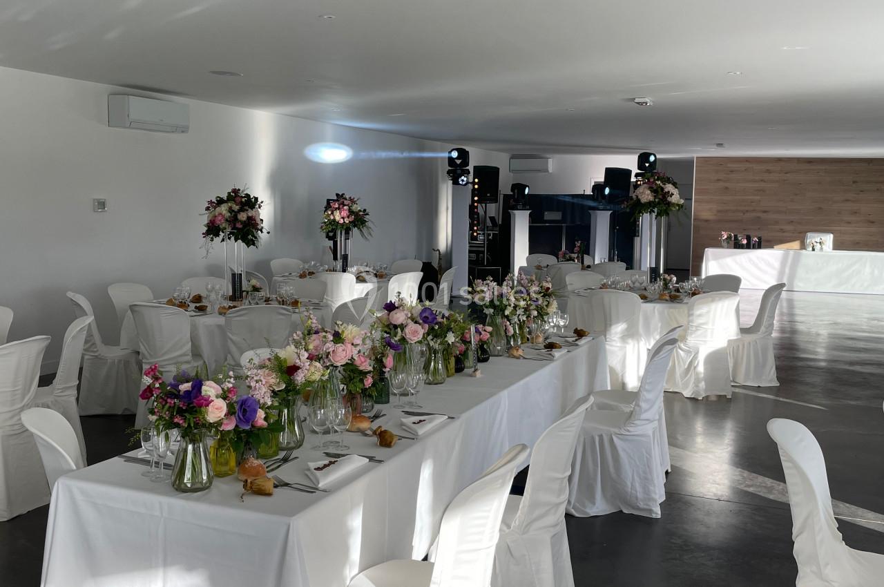Salle de réception décorée avec des tables blanches, des bouquets de fleurs colorées et une lumière naturelle.