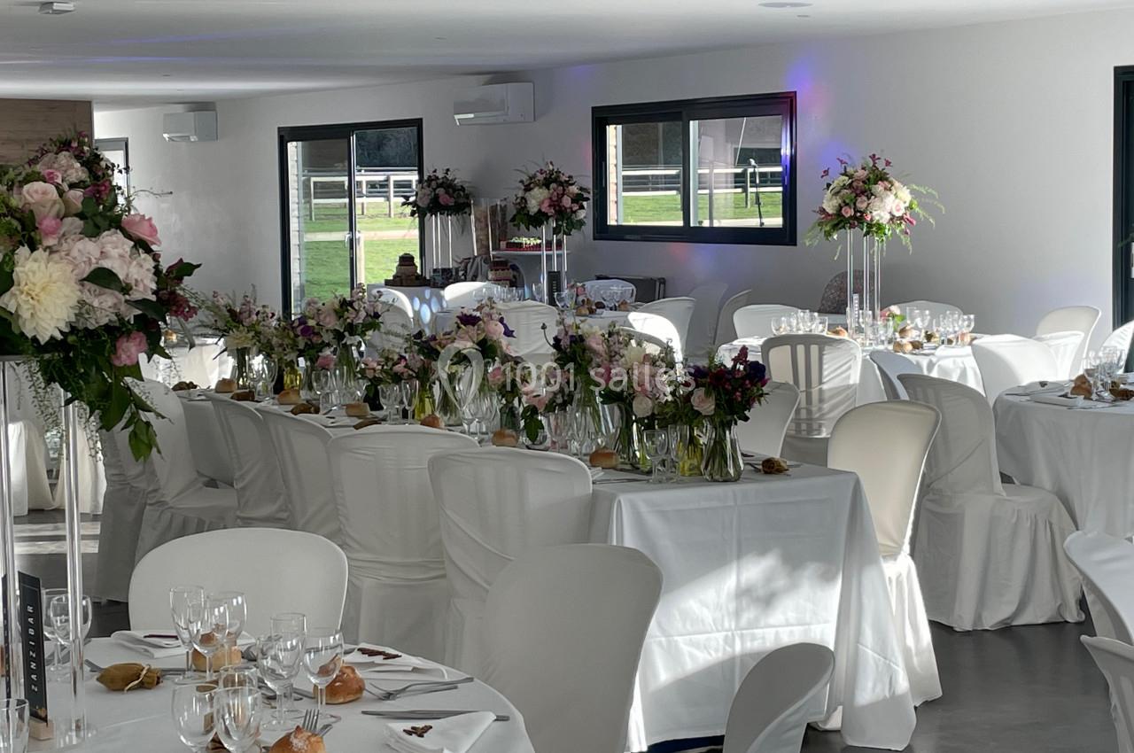 Salle de réception décorée pour un mariage, avec tables dressées, nappes blanches et arrangements floraux élégants.