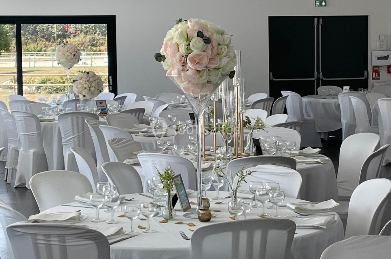 Salle de réception décorée avec des tables rondes, nappes blanches et centres de table floraux élégants.