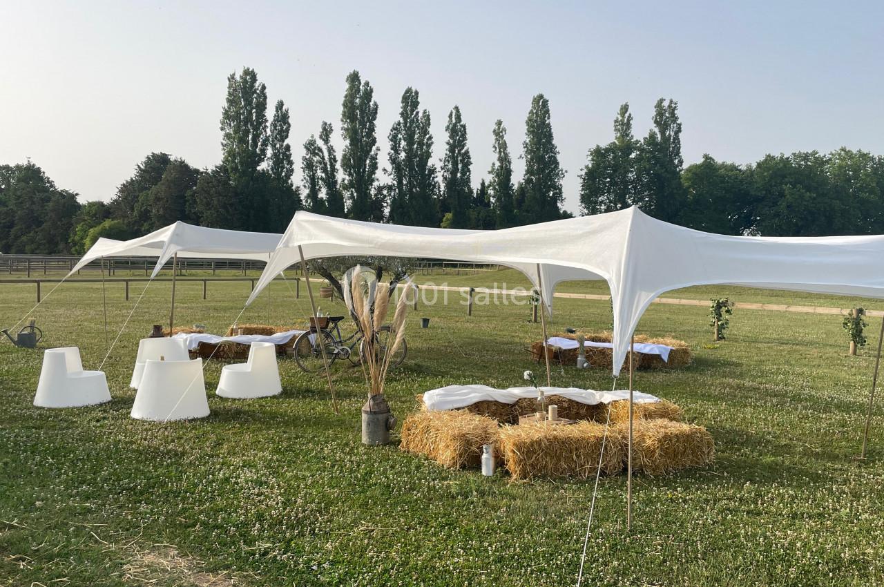 Tentes blanches montées sur une pelouse avec des bottes de paille disposées en sièges autour de tables basses.