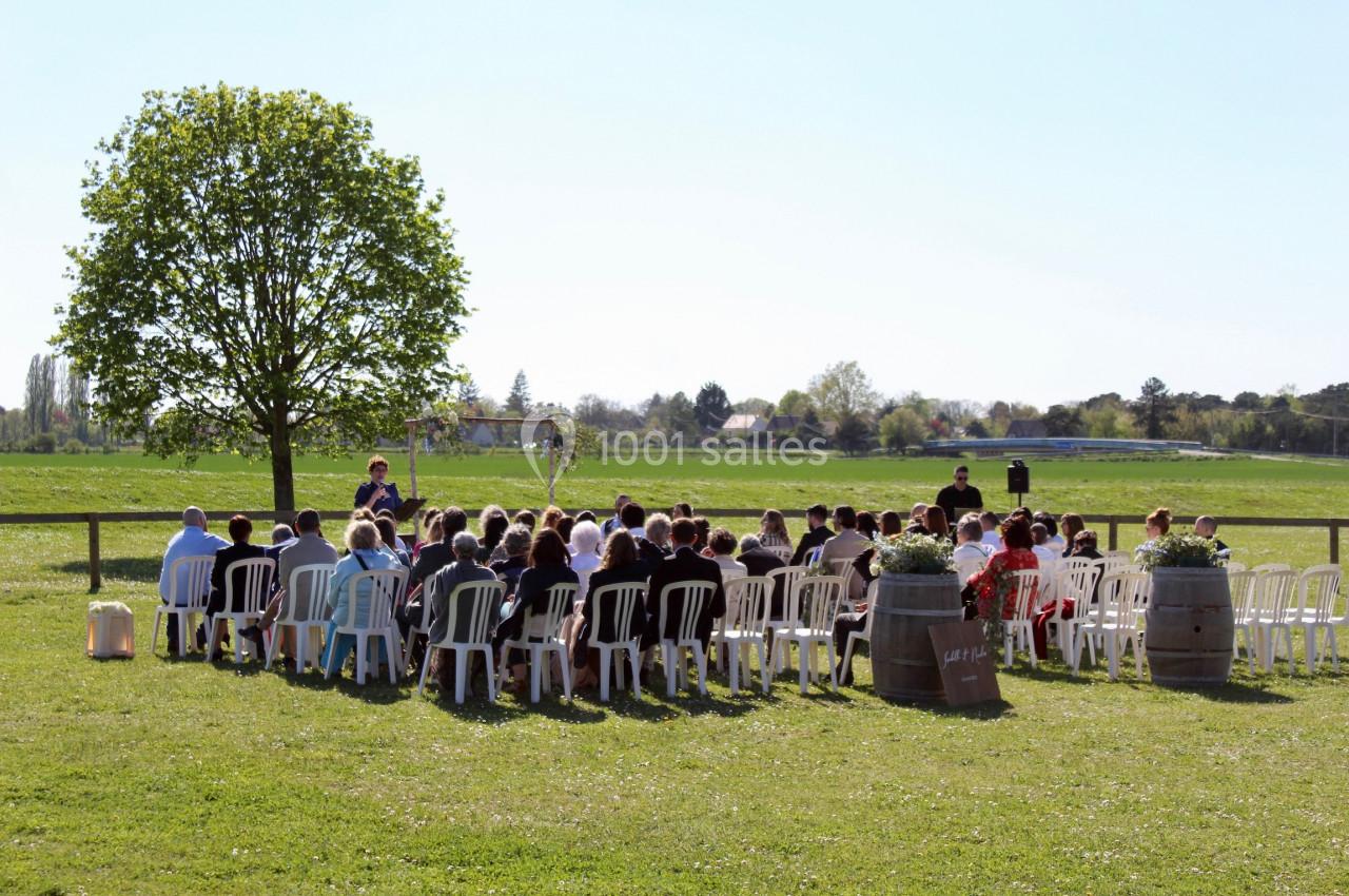 Un groupe de personnes assises en plein air lors d'une cérémonie, avec un arbre et un champ en arrière-plan.