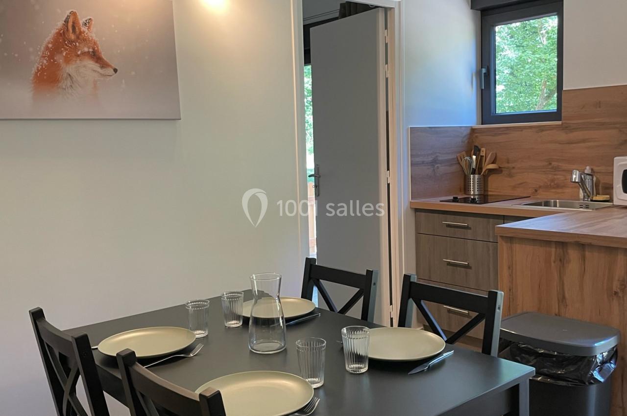 Table noire dressée pour quatre personnes dans une cuisine moderne avec meubles en bois et tableau mural représentant un…
