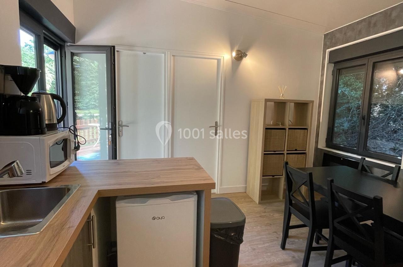 Cuisine compacte avec plan de travail en bois, réfrigérateur, micro-ondes, cafetière et table à manger près d'une fenêtre.