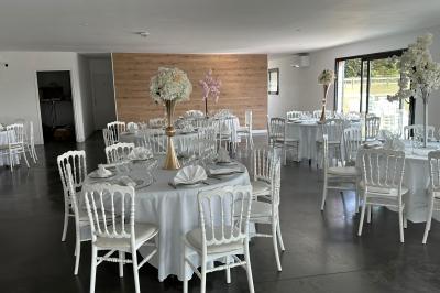 Salle de réception lumineuse avec tables rondes décorées de nappes blanches, fleurs et vaisselle élégante.