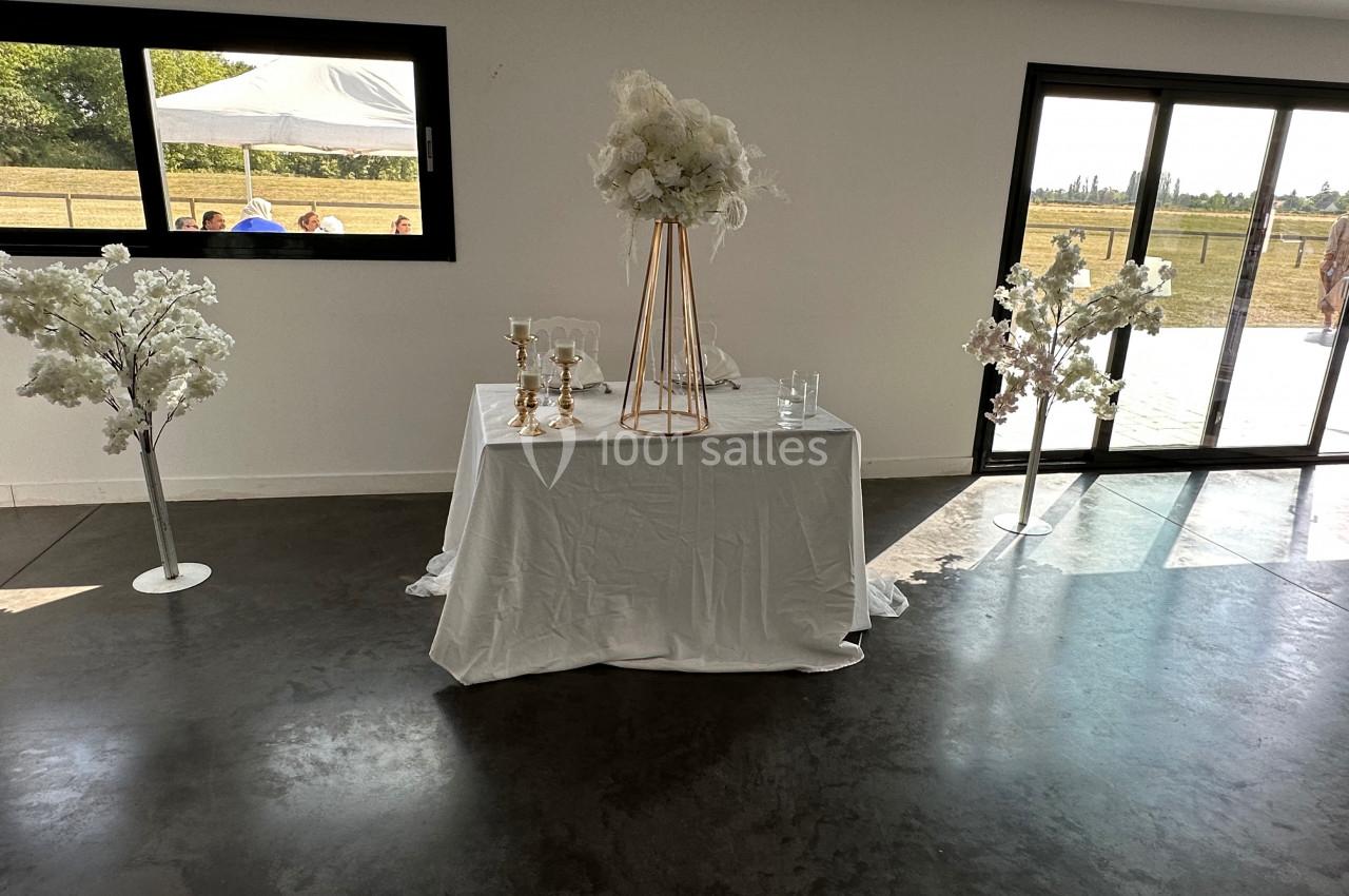 Table décorée avec une nappe blanche, des chandeliers dorés et un bouquet de fleurs blanches, dans une salle lumineuse.
