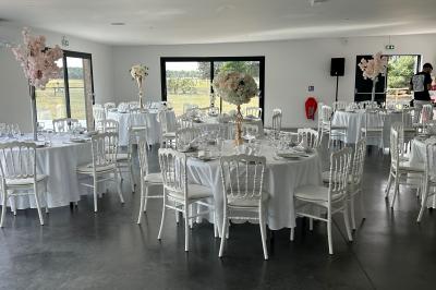 Salle de réception lumineuse avec tables rondes décorées de nappes blanches, fleurs et vaisselle élégante.