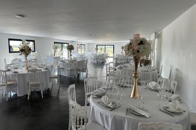 Salle de réception lumineuse avec tables rondes décorées de nappes blanches, fleurs et vaisselle élégante.