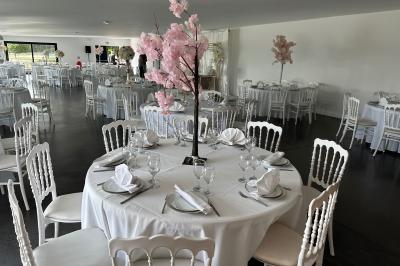 Salle de réception lumineuse avec tables rondes décorées de nappes blanches, fleurs et vaisselle élégante.